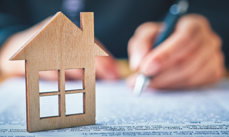 person filling out an insurance claim form with miniture wooden house outline