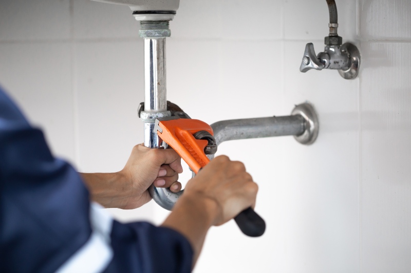 Plumber fixing white sink pipe with adjustable wrench